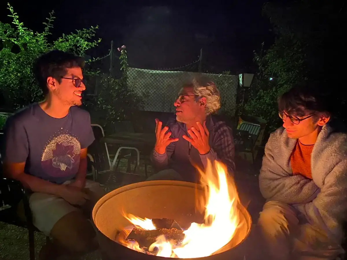 Three people talking around a fire bowl at night